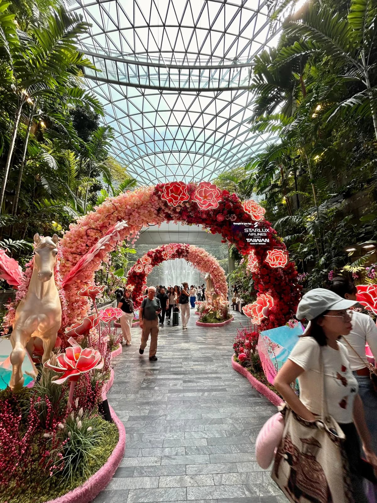 Neon-lit pink and red floral arches with white horse statues in the Jewel Changi garden display