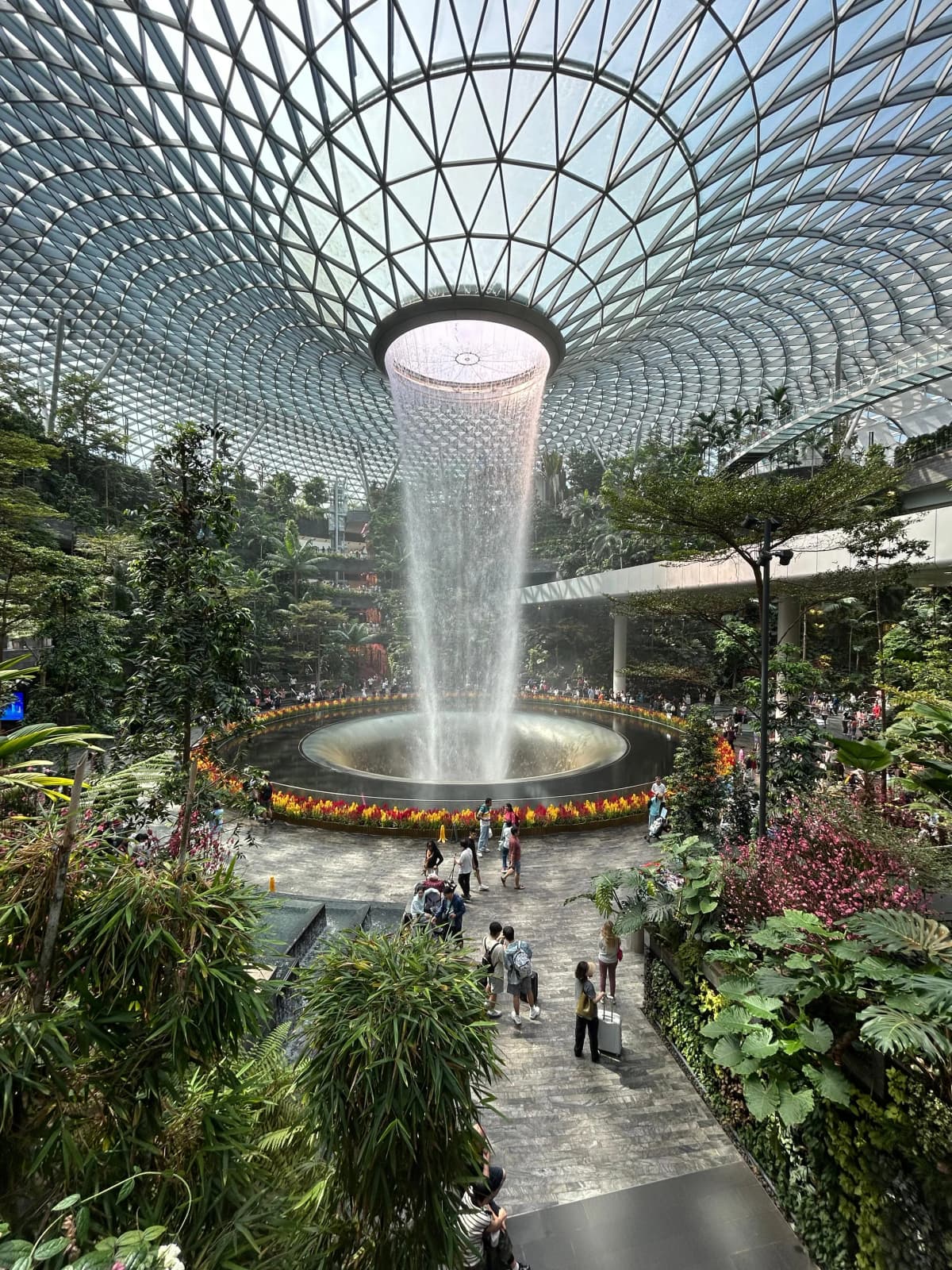 The HSBC Rain Vortex waterfall pouring through the glass roof of Jewel Changi Airport, surrounded by a terraced indoor forest